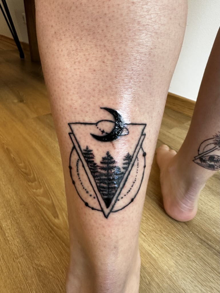 Tattoo on leg of trees inside a double triangle with crescent moon above and dotted circle around.