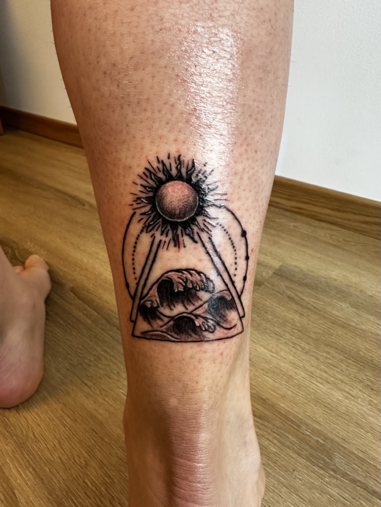 Tattoo on leg showing a sun above a triangle containing three seashells on skin.