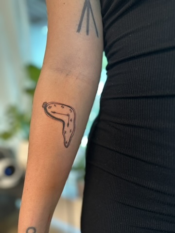 Arm tattoo of a melting clock inspired by Salvador Dalí's surreal art.
