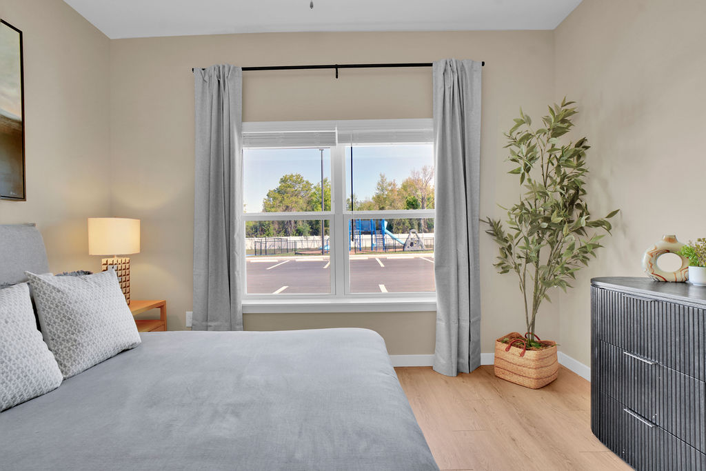 Bedroom with bed, dresser, plant and large window