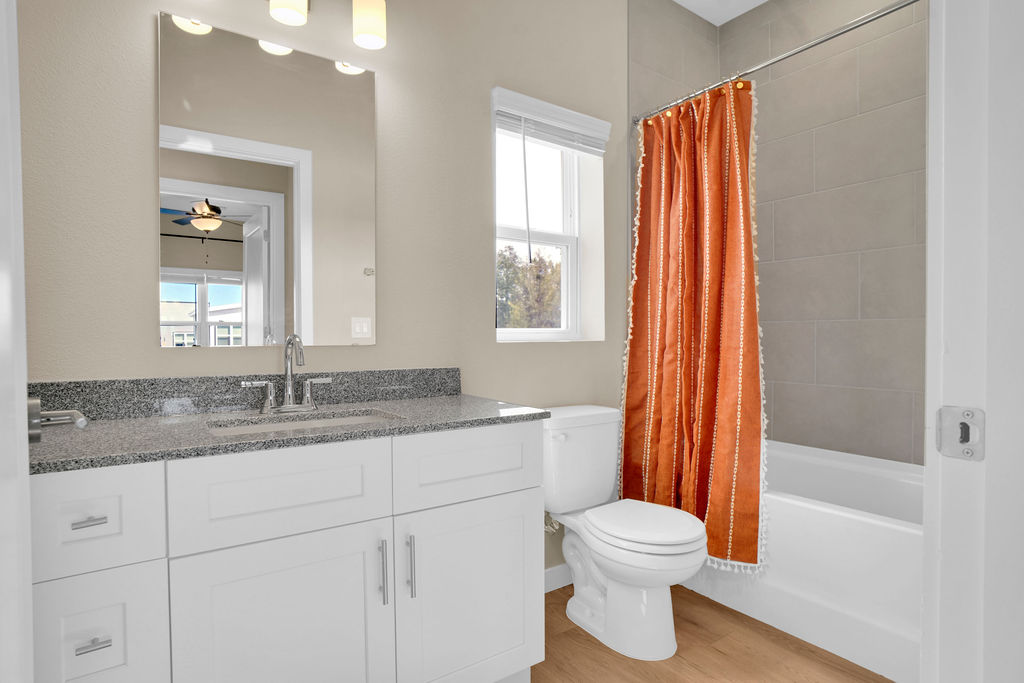 Bathroom with tiled garden tub, white cabinets, grey granite countertop, window and shower curtain