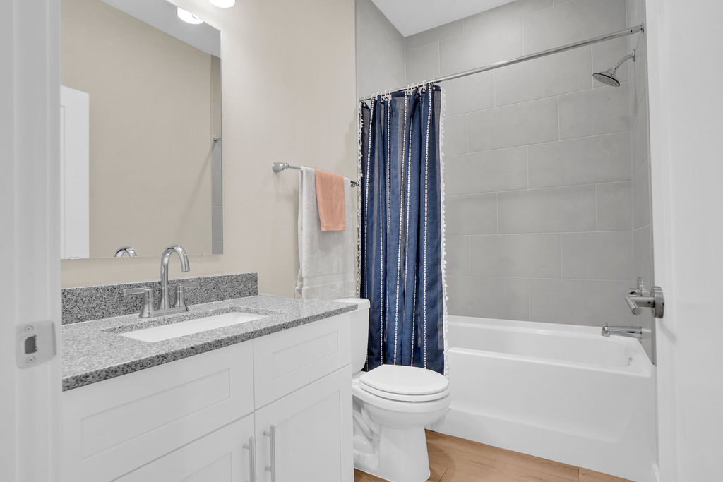Bathroom with garden style tub, shower curtain, white cabinets, grey granite countertops