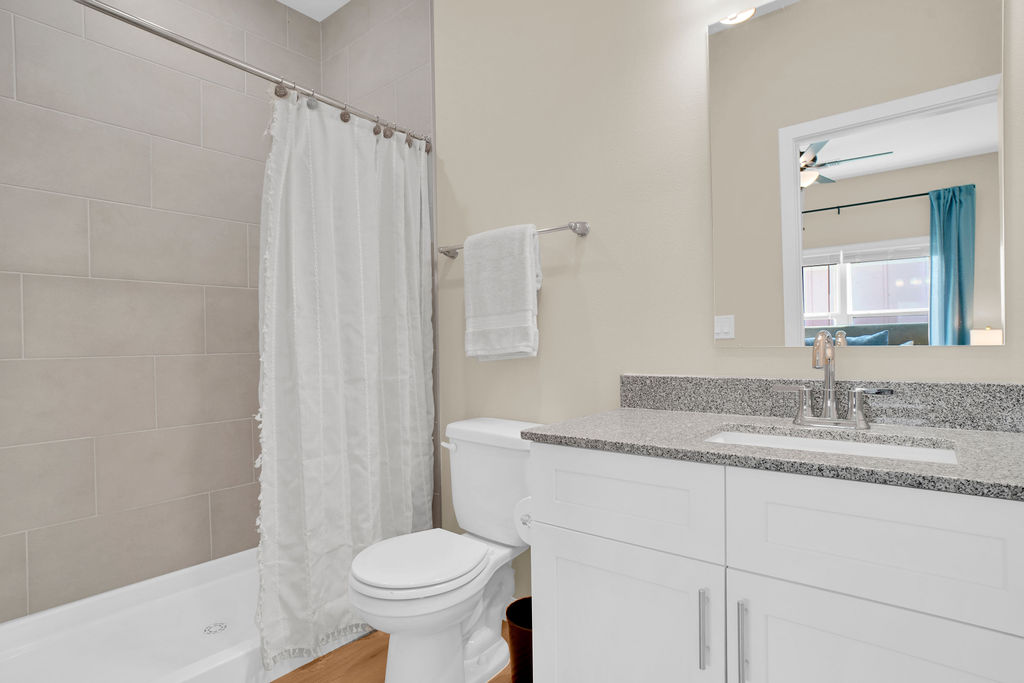 Bathroom with tiled garden tub, white cabinets, grey granite countertop, window and shower curtain