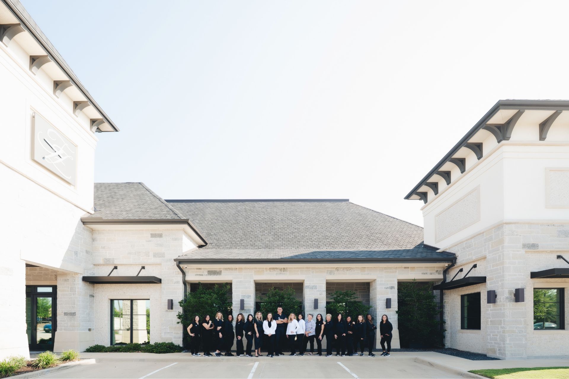 Group of 19 women standing in front of a modern stone building with large windows under clear sky.