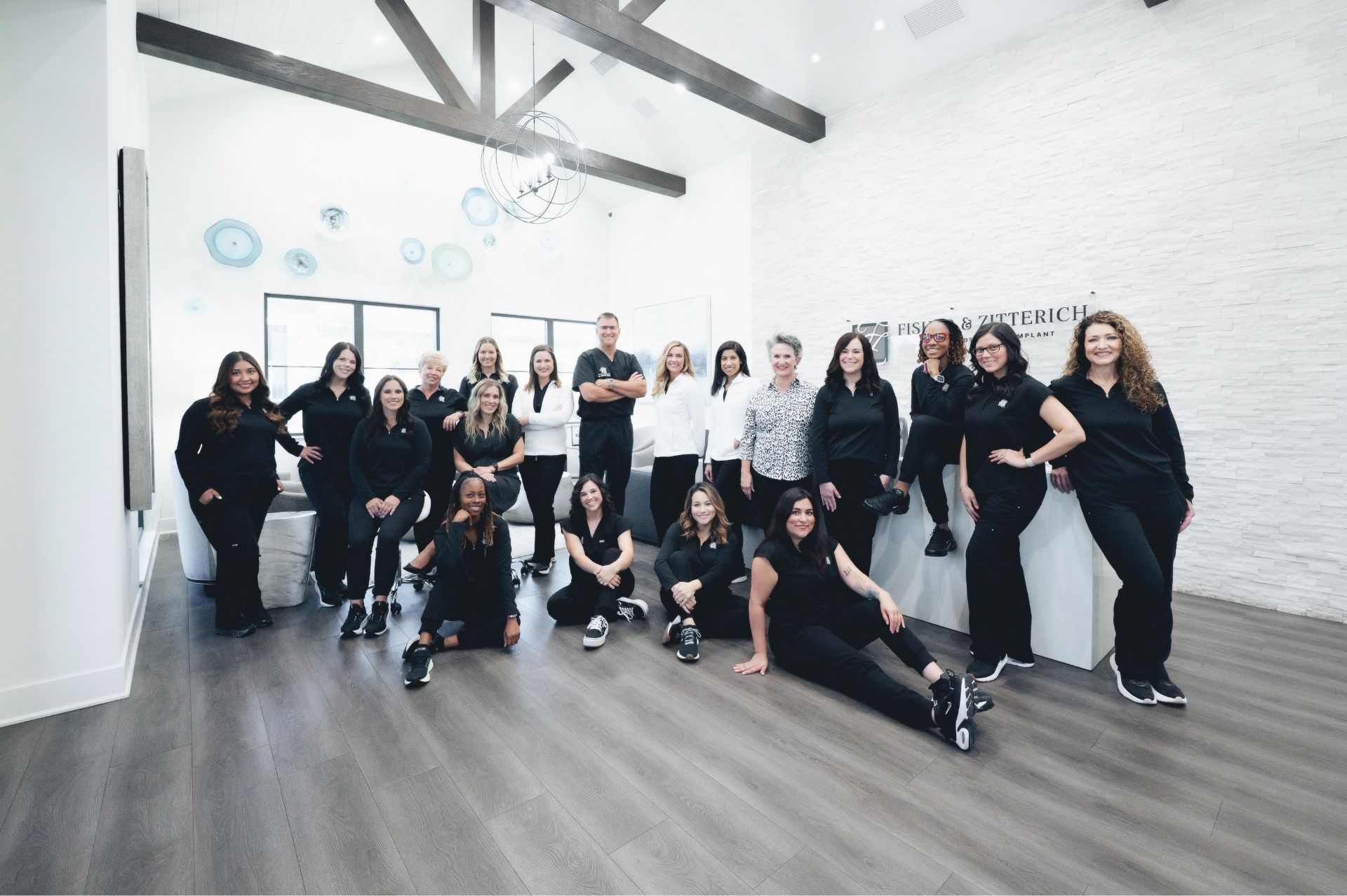 Group photo of a diverse team of 17 people posing in a modern office with high ceilings and wooden beams.