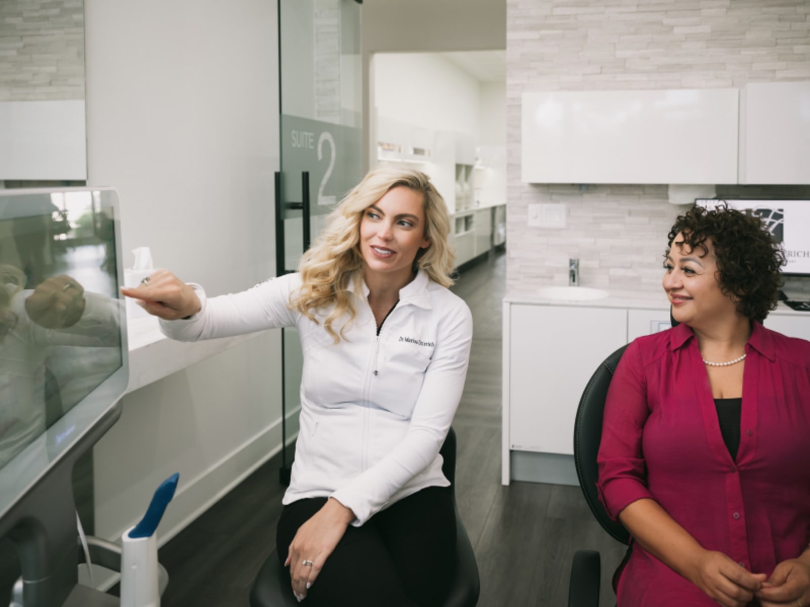 A dental professional discussing care with a patient in a modern dental office treatment room.
