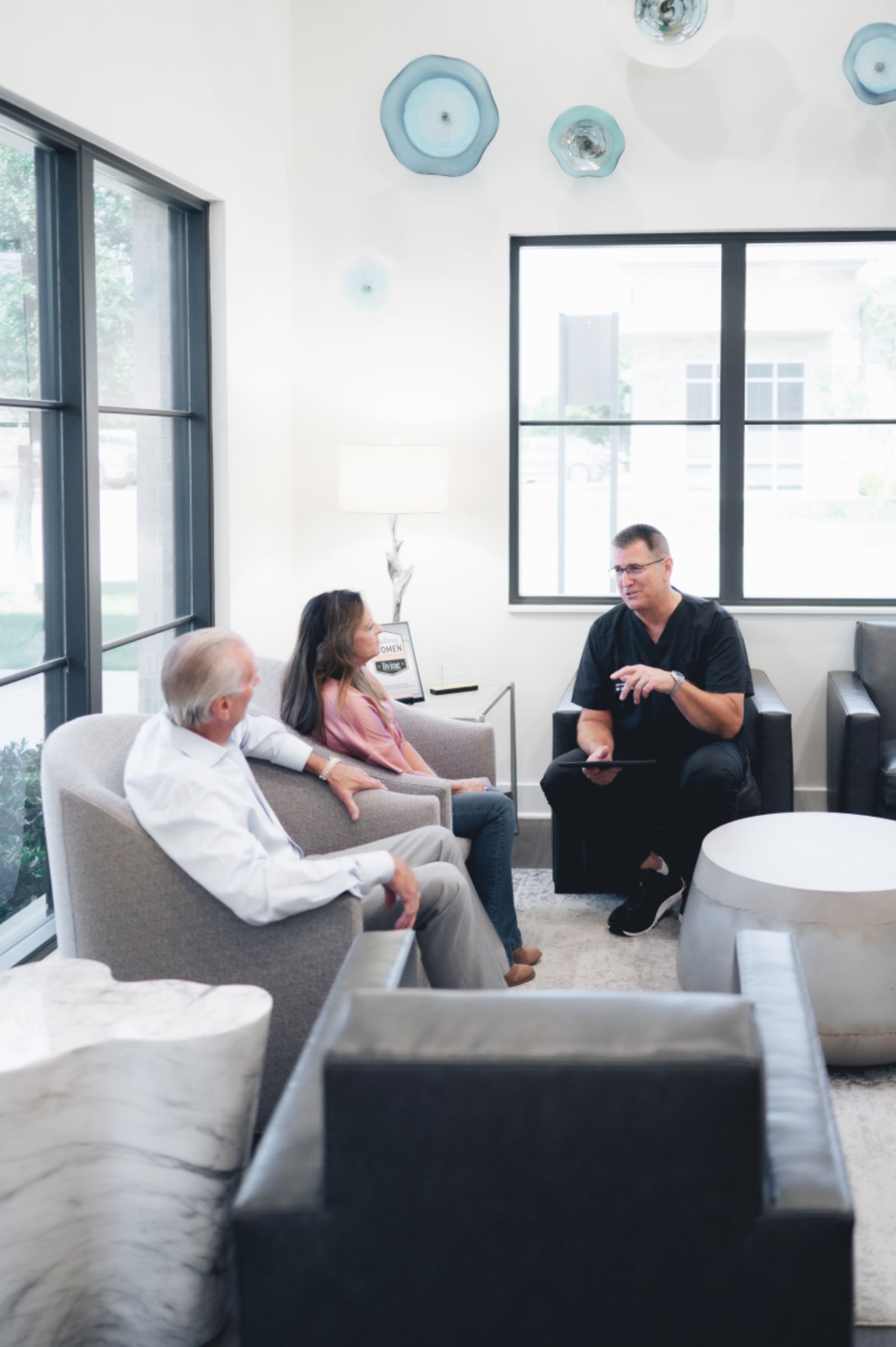 Dental team member speaking with patients in a modern, bright office waiting area.