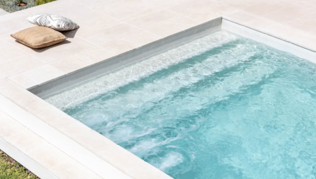 Sapphire fibreglass pool with tanning ledge and light-toned paving