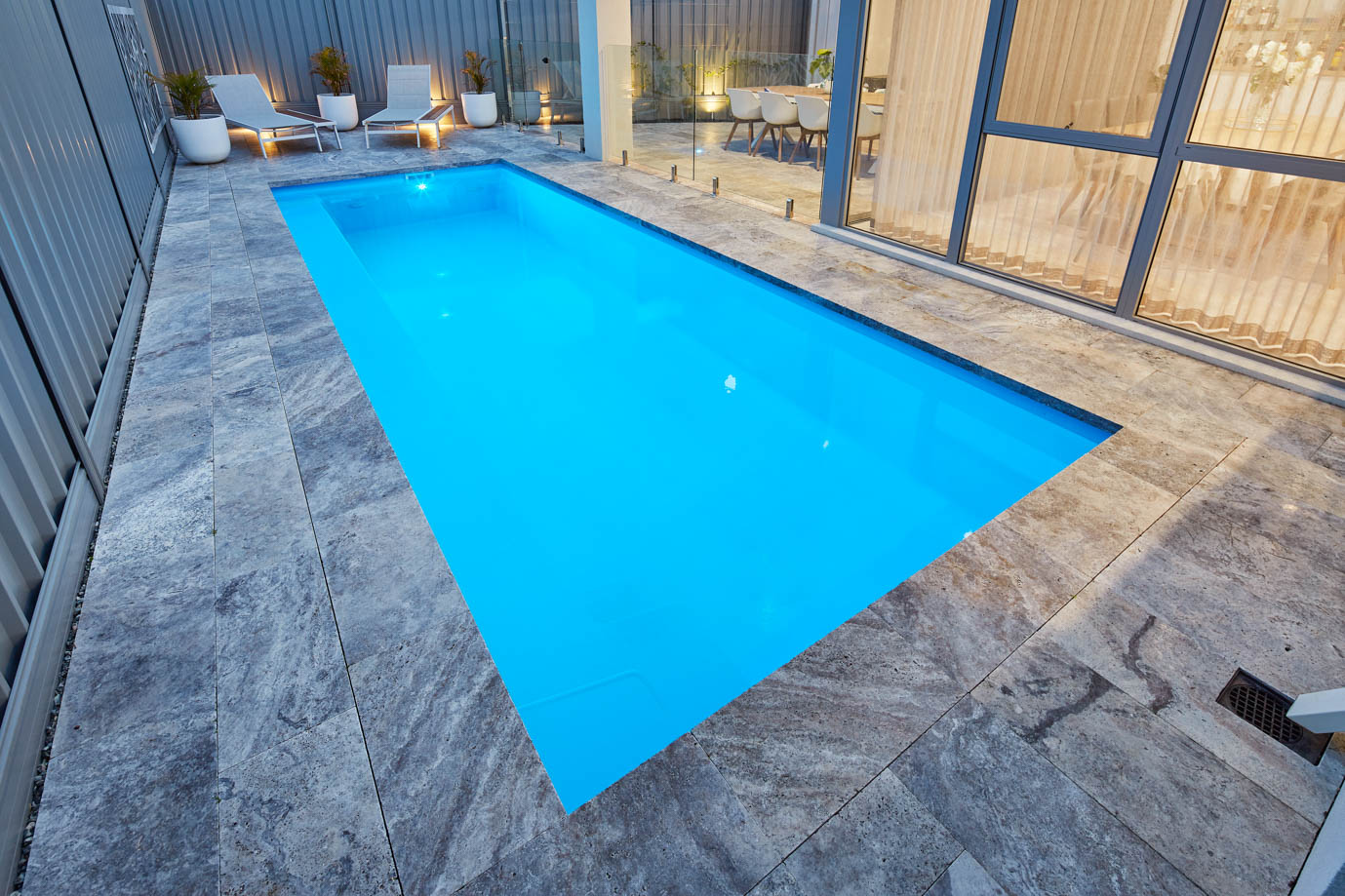 Imperial fibreglass pool on a grey stone terrace with outdoor seating