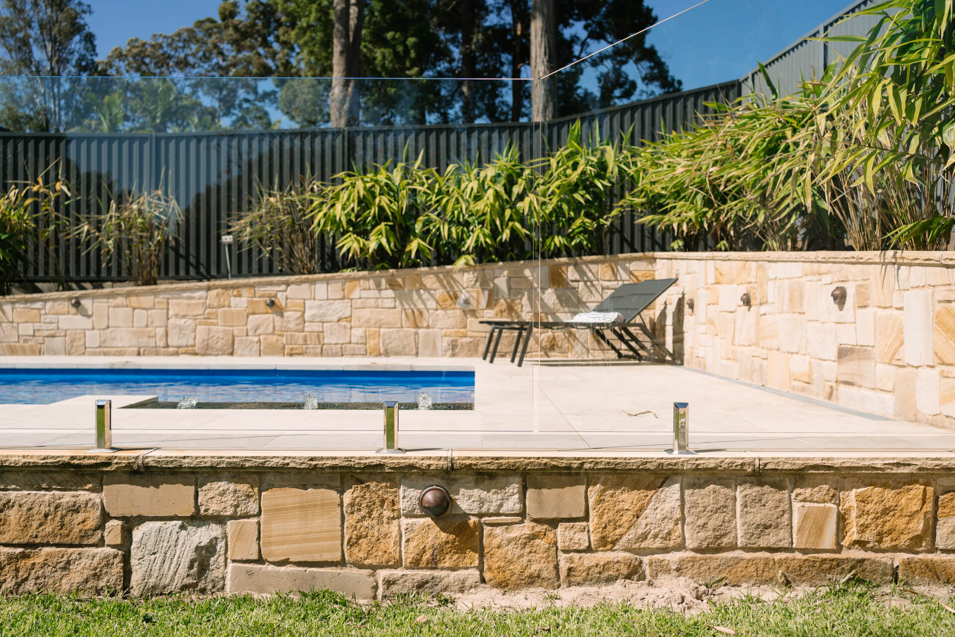 President fibreglass pool in Mediterranean with sandstone retaining walls and black fencing