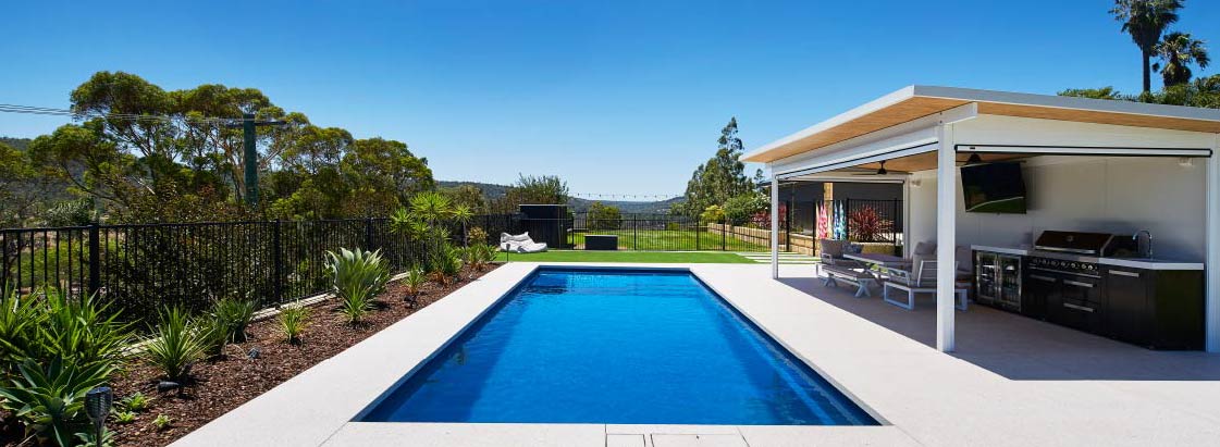 Family backyard fibreglass pool beside an alfresco area with outdoor kitchen
