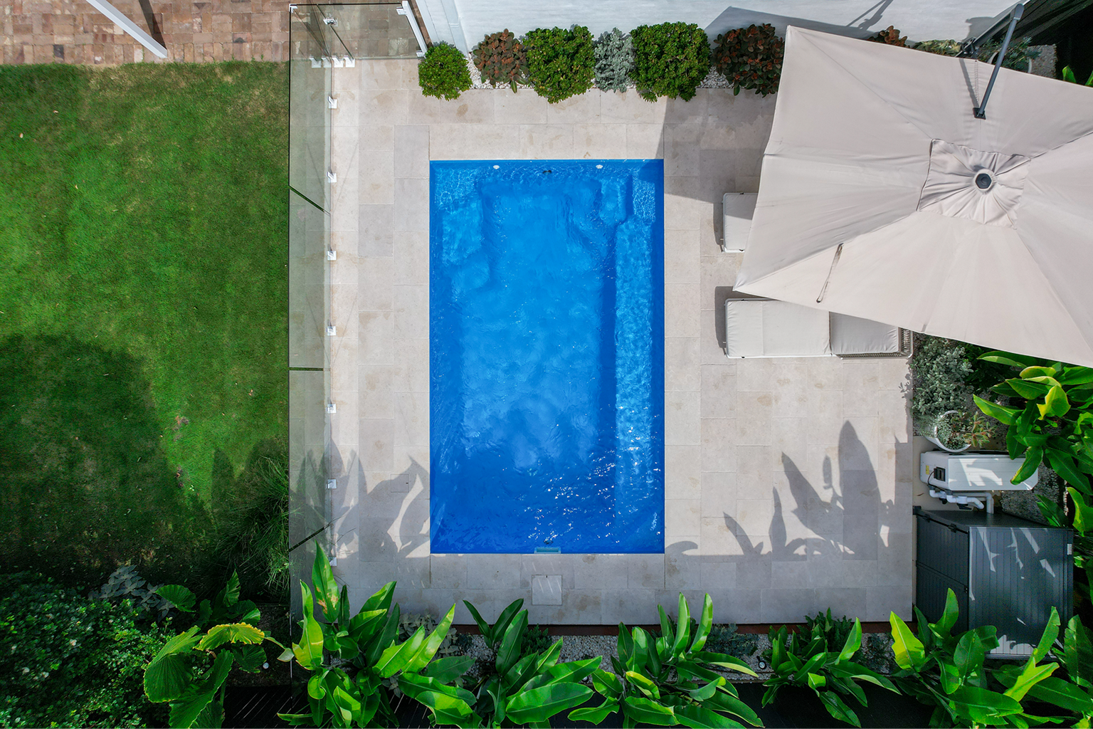 Aerial view of a backyard pool with cantilevered umbrella and tropical gardens