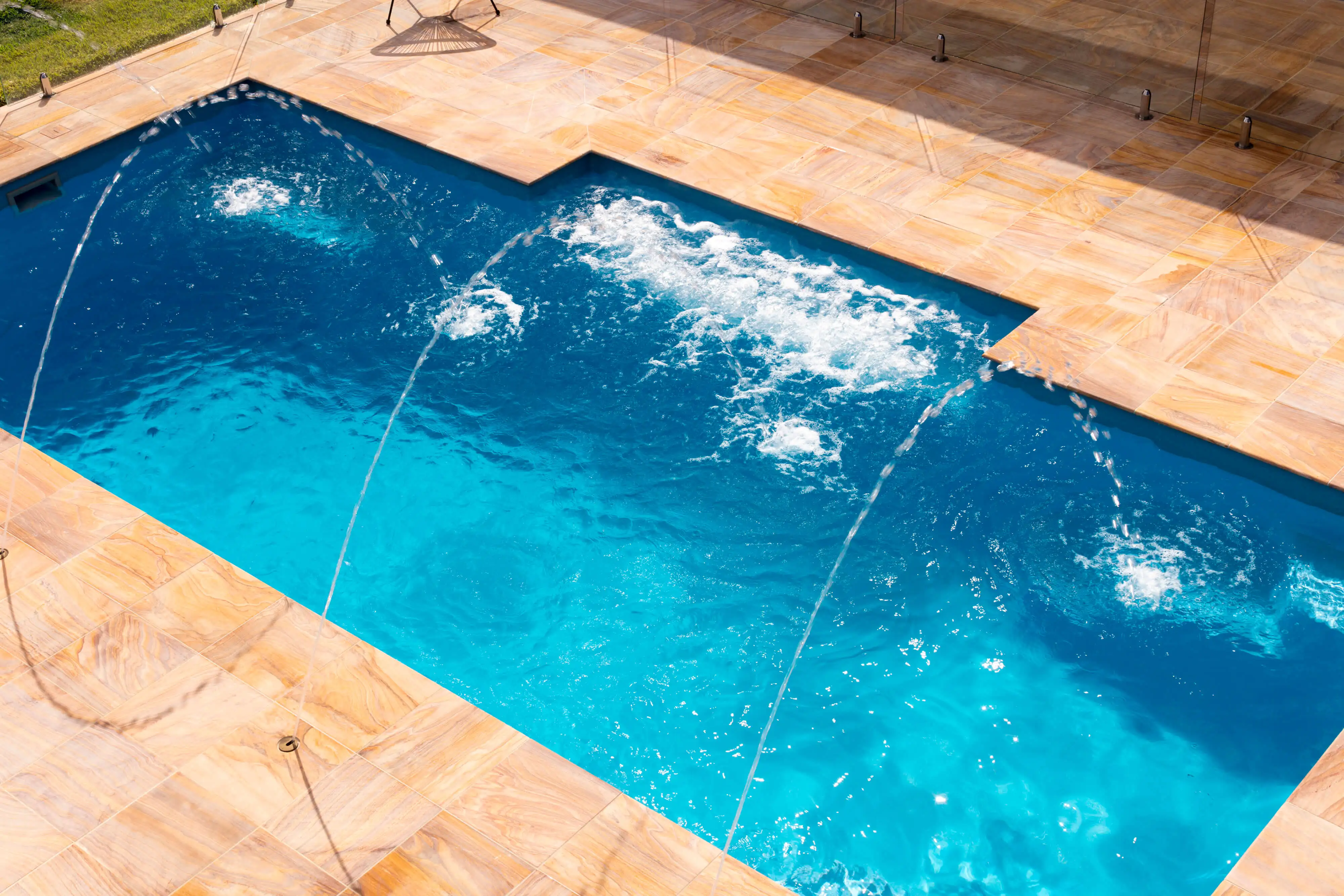 Deck jets arcing into a Senator fibreglass pool with sandstone paving, view 1