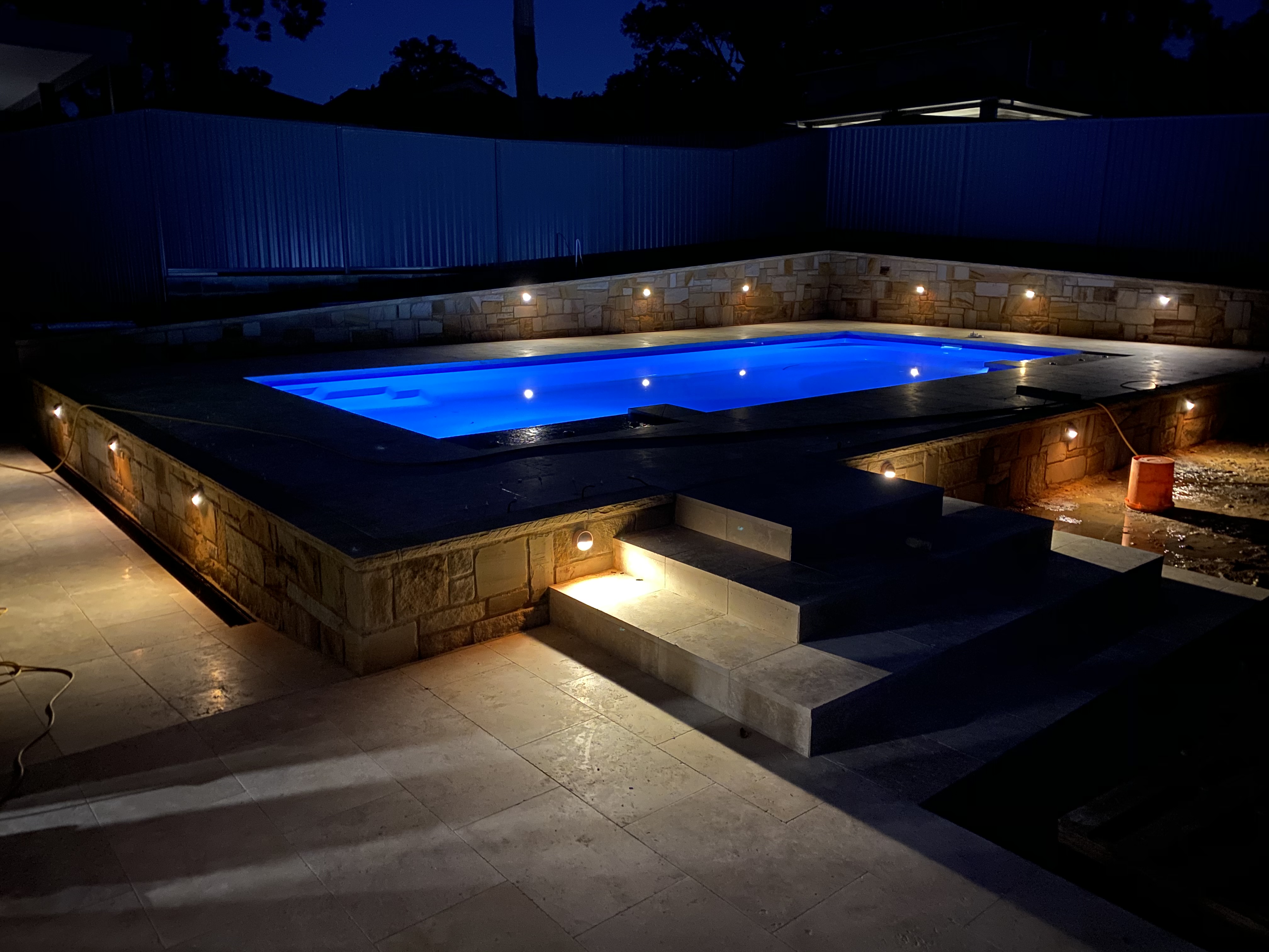 Raised fibreglass pool with stone walls and landscape lighting at night