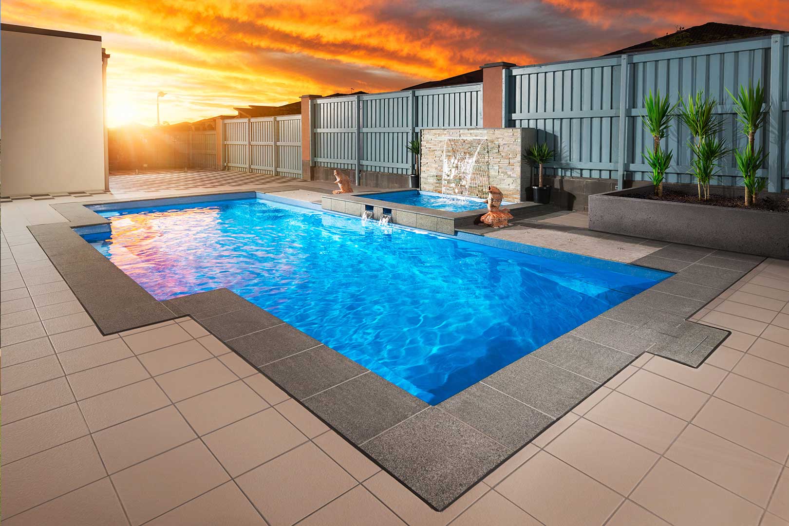 Crystal Blue fibreglass pool at sunset with charcoal tile border and water feature wall