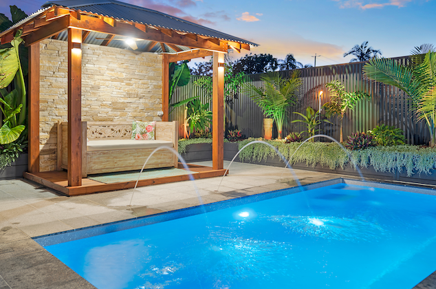 Fibreglass pool at dusk with timber cabana, stone feature wall and deck jets