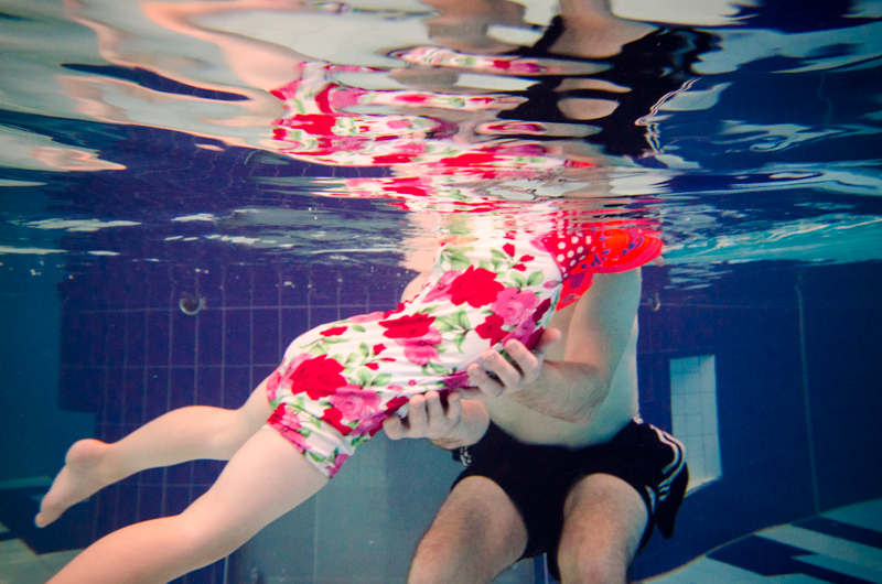 Underwater view of a young child swimming with assistance from an adult