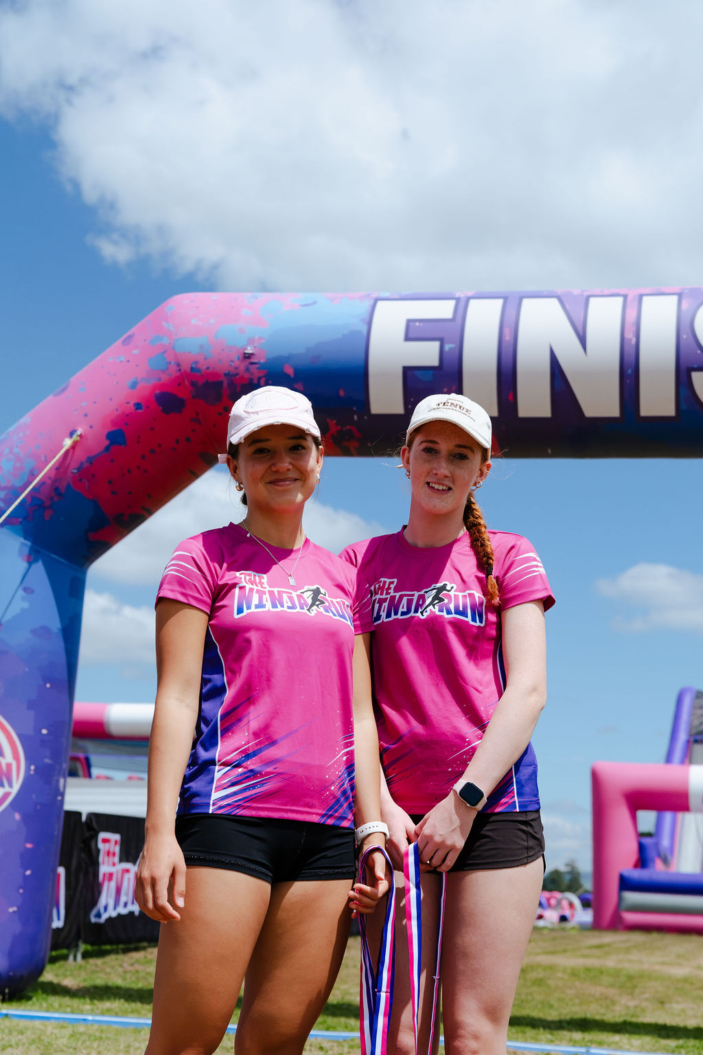Two crew members in pink shirts smiling at the finish arch