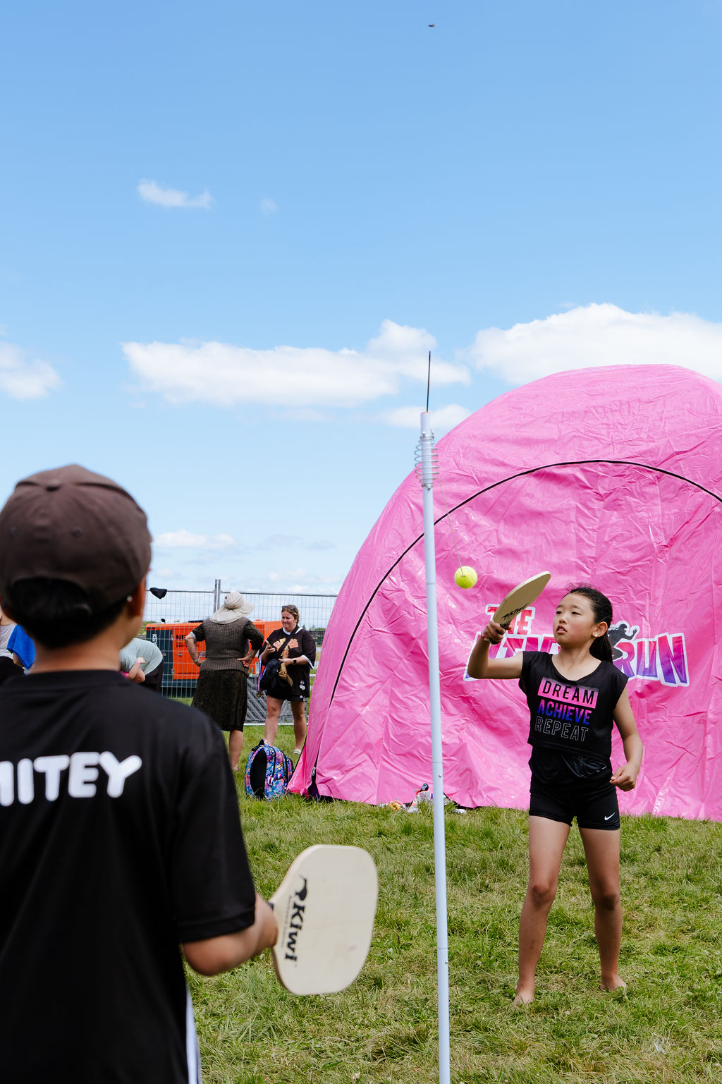 Kids playing swingball beside a pink event tent