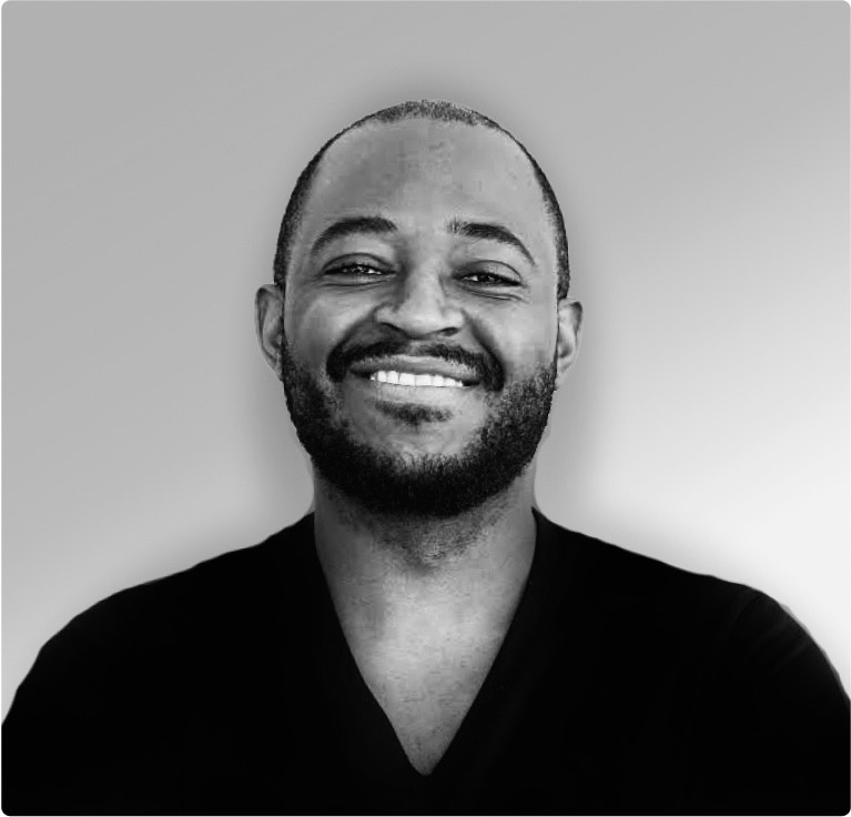 Portrait en noir et blanc d'un homme souriant avec une barbe et une chemise noire à col en V.