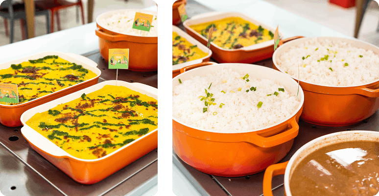 Vários recipientes laranjas com arroz branco decorado com ervas, feijão e uma lasanha coberta com molho verde e dourado em uma bancada.