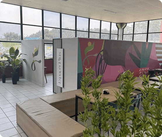 Ambiente interno de escritório com paredes coloridas com arte abstrata, plantas em vasos e áreas de assento com sofás e mesas.
