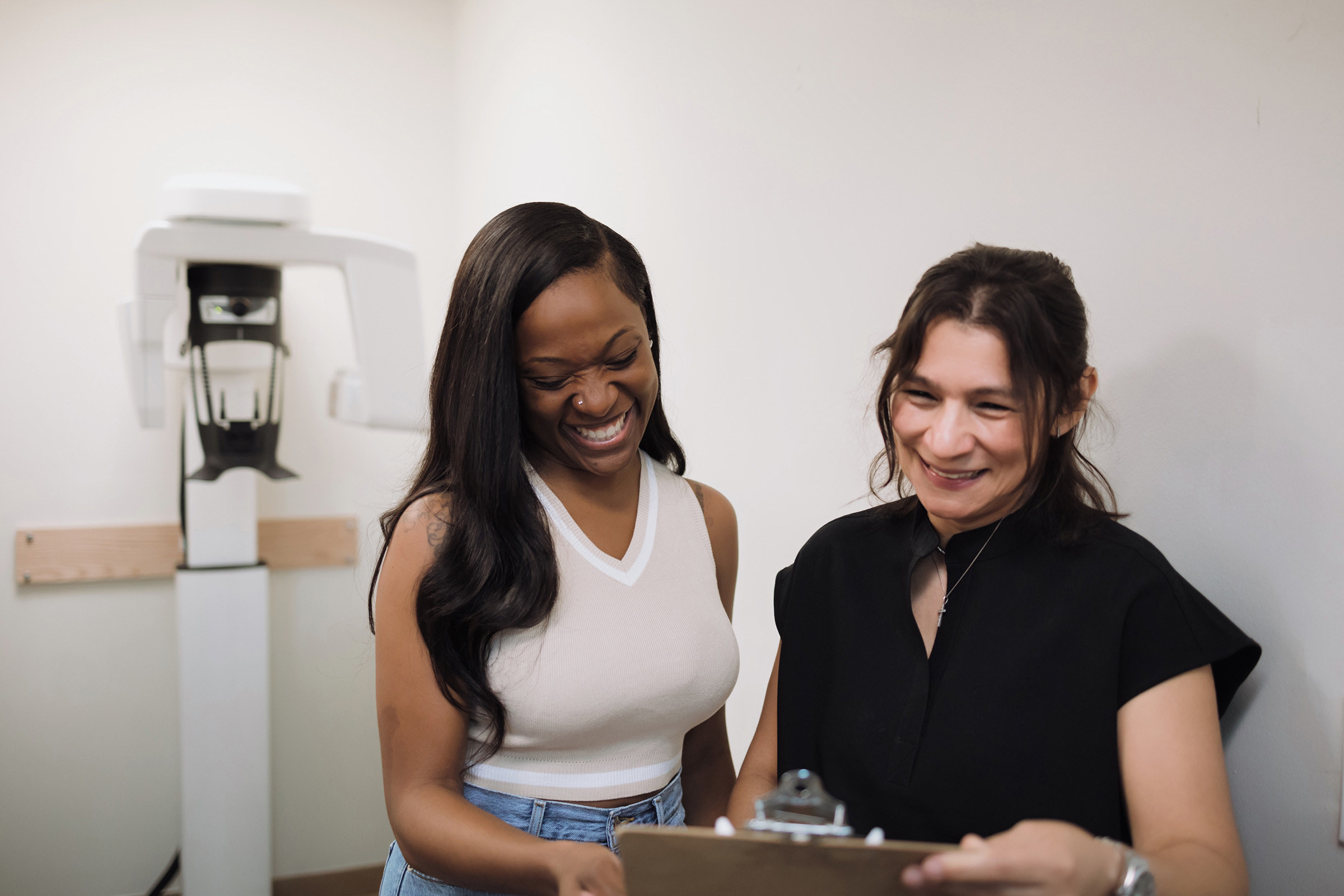 Two women smiling and looking at a clipboard in a medical or dental office.