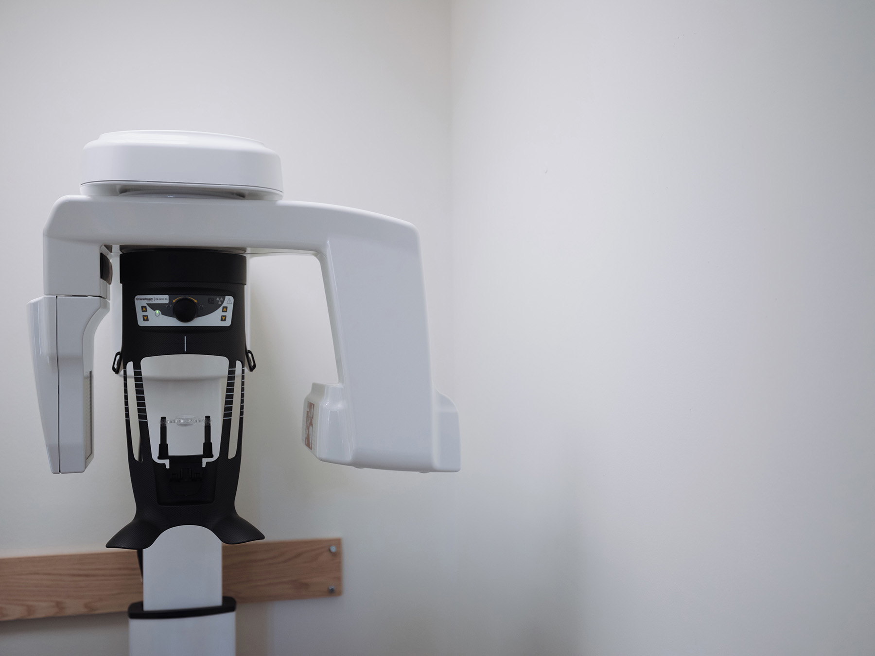 Dental panoramic X-ray machine with white walls and a wooden panel behind it.