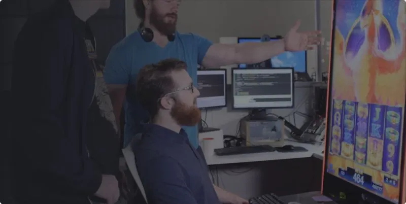 AGS developers discussing code with game screen and multiple monitors