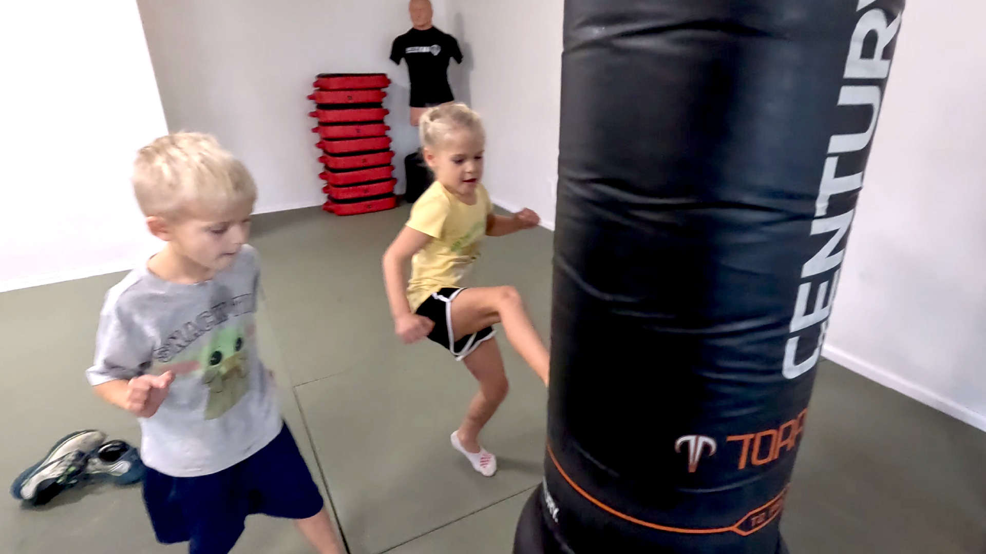 Two kids kicking a punching bag.