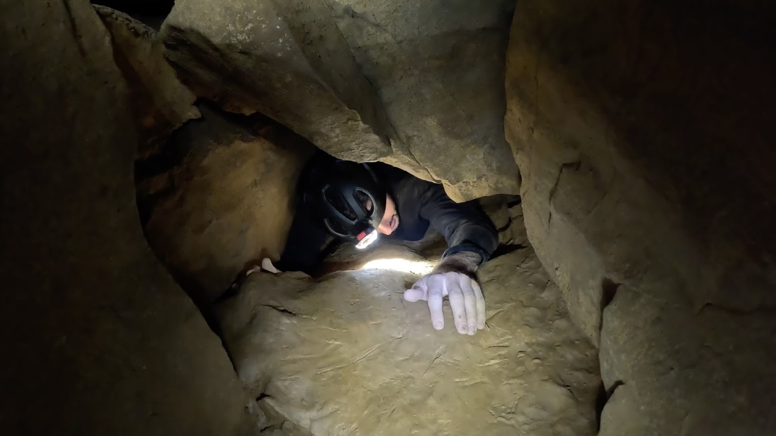 Man crawls through a gap in a cave