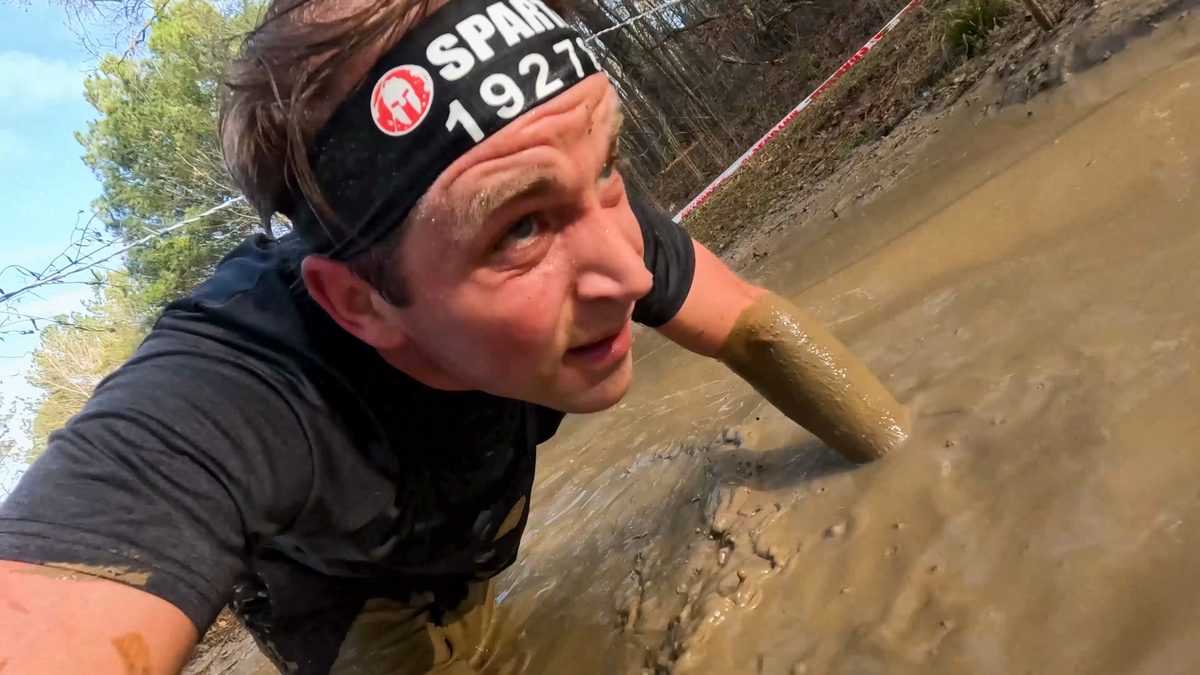 Man crawls through mud obstacle