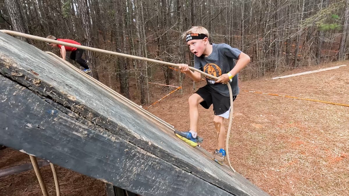 Kid climbs wall with rope in race