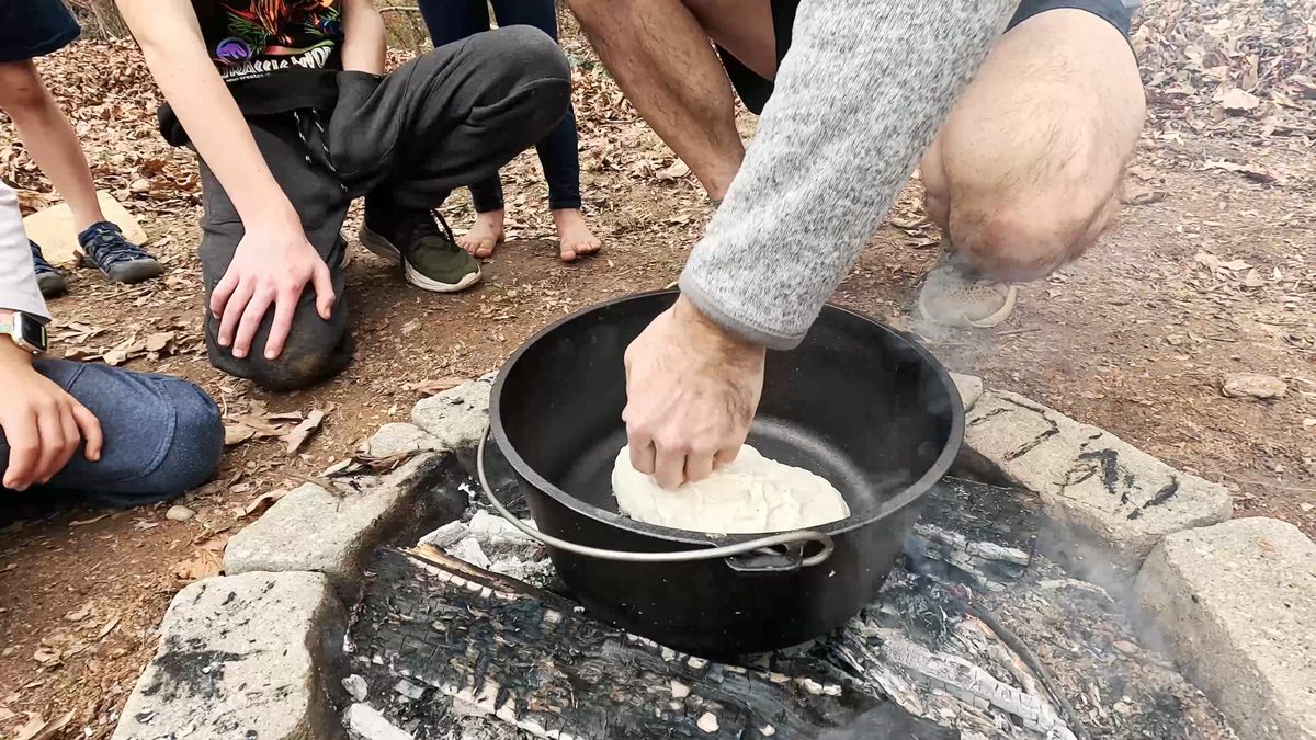 Adding dough to pot on campfire
