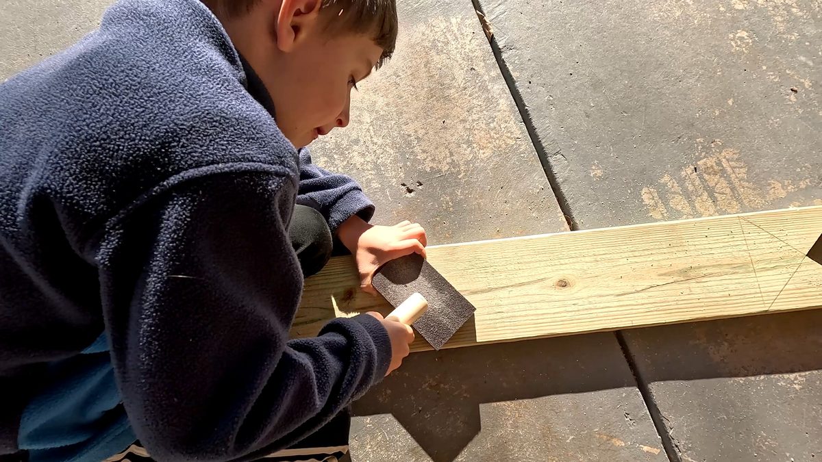 A boy sands a wood piece