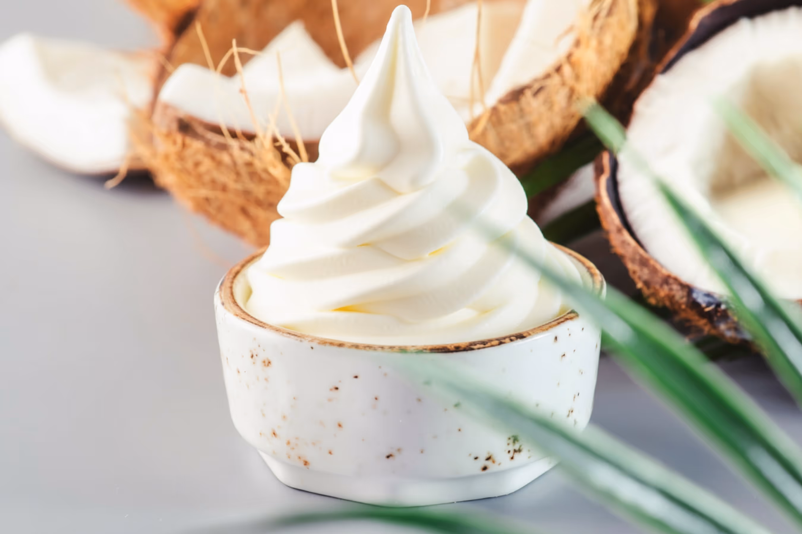 Swirled soft serve ice cream in a white ceramic cup with halved coconuts in the background.