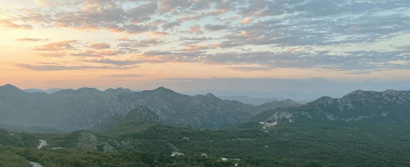 Mountain range under a partly cloudy sky with a sunset glow on the horizon.
