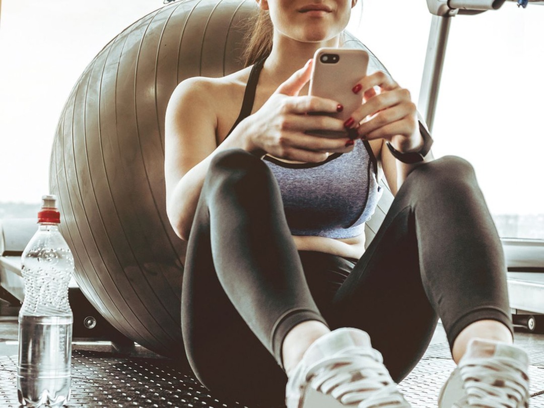 woman sitting and using a phone one - Free Workout Apps For Women