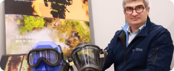 Man in glasses and blue jacket posing with snorkeling and diving masks on a table.