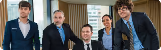 Five diverse professionals in business attire smiling in a modern office setting.