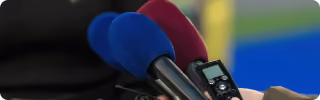 Close-up of three microphones with covers, including blue and red, held near a person for recording.