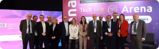 Group of 13 professionally dressed people posing in front of a Tech Inno Arena event backdrop.