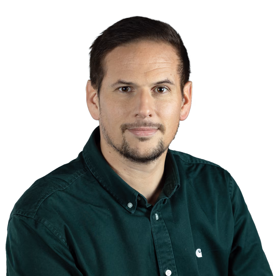 Man with short dark hair and beard wearing a green buttoned shirt against a gray background.