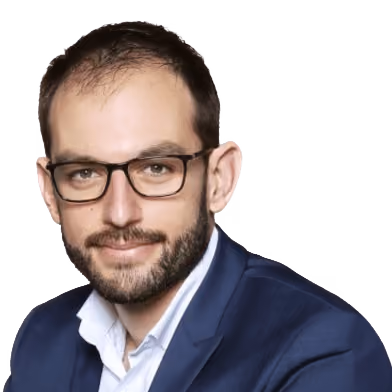 Man with glasses and beard wearing a navy suit and white shirt against a gray background.