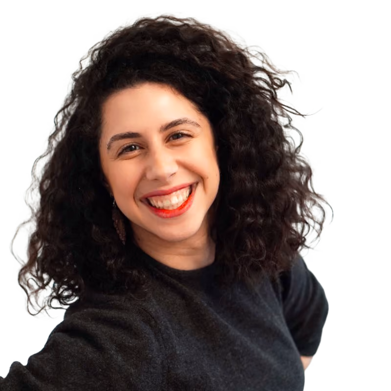 Smiling woman with curly dark hair, wearing a black top and red lipstick against a light background.