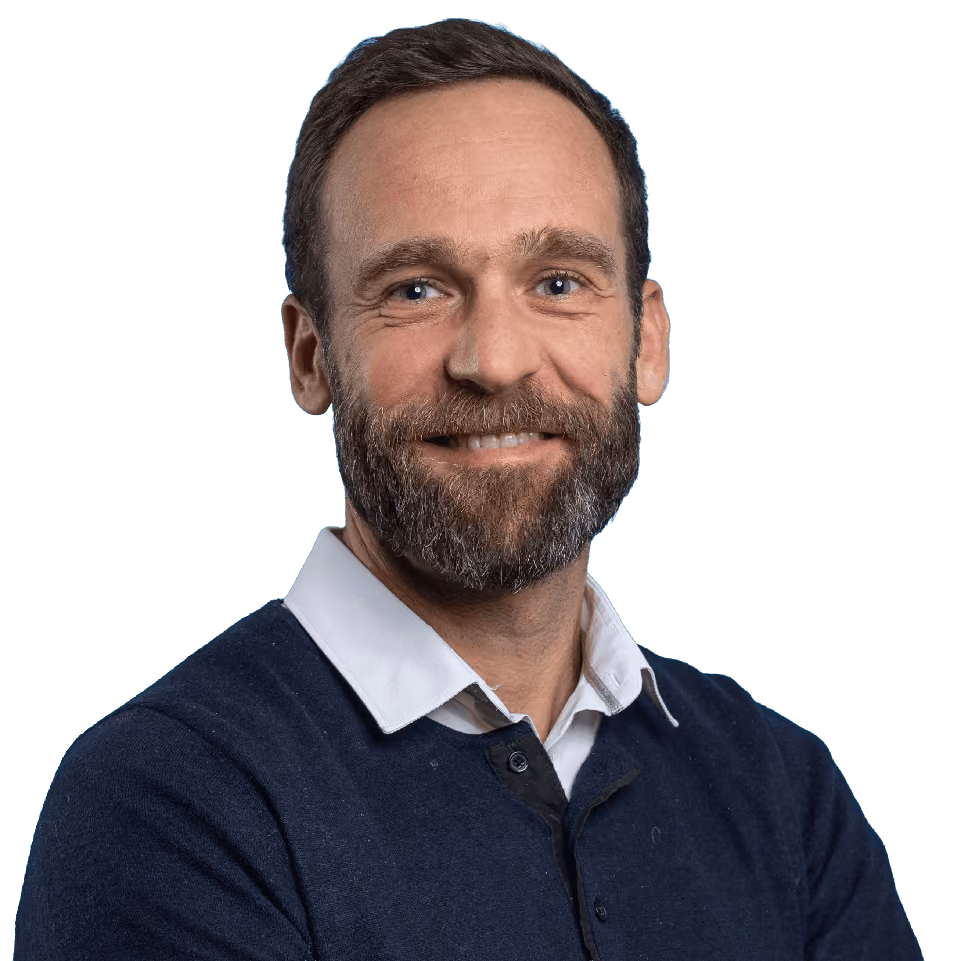 Smiling man with beard wearing white collared shirt under dark blue sweater.