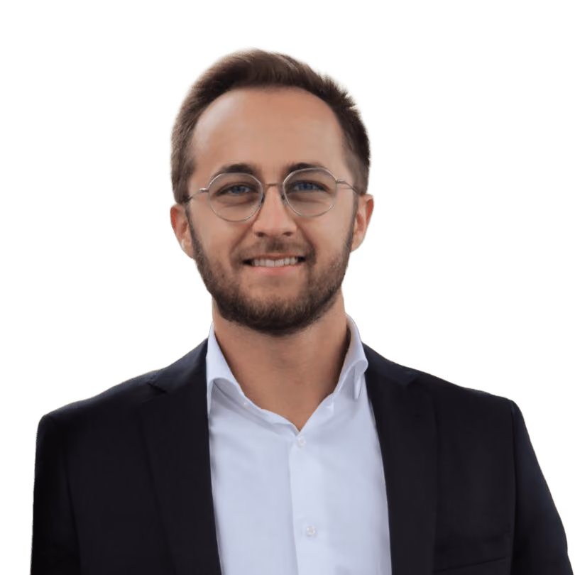 Smiling young man with glasses wearing a black suit jacket and white shirt.
