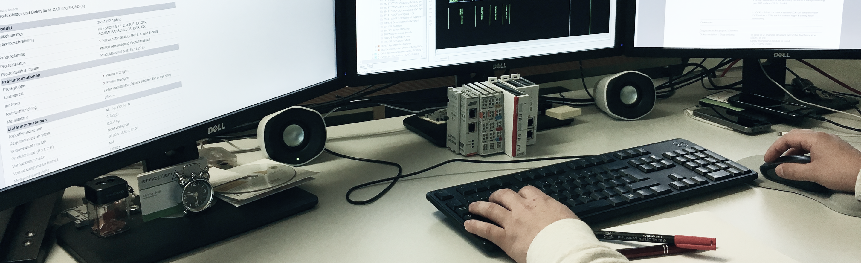 Hände an Tastatur und Maus vor zwei Monitoren, daneben eine Steuerungsbaugruppe