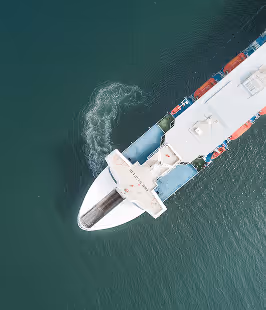 Aerial view of a ship's bow cutting through calm water with a small wake swirling nearby.