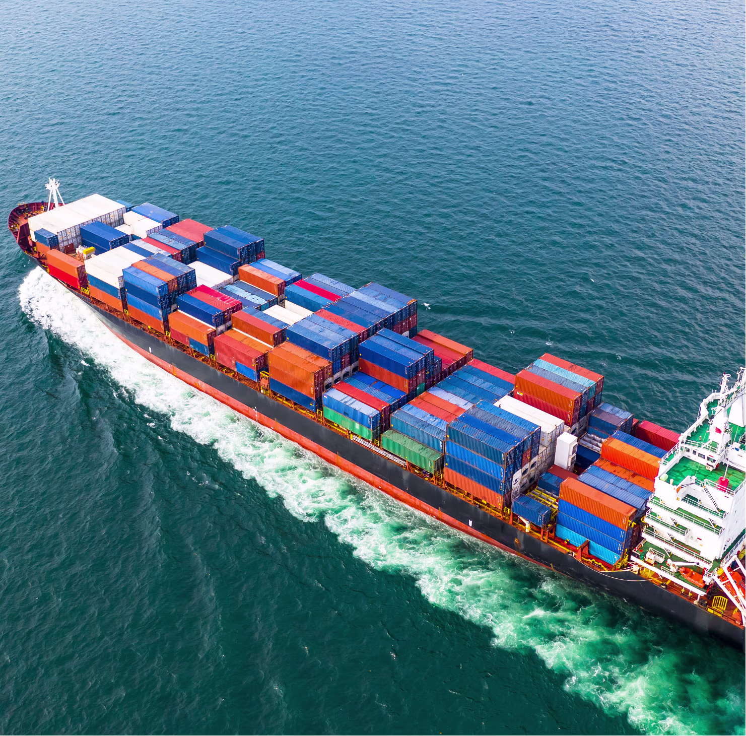 A large cargo ship loaded with multicolored shipping containers sailing through blue ocean water.